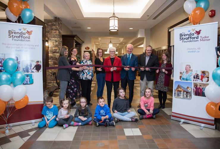 <p>Pictured at the official ribbon-cutting Nov. 22, 2018, back row from left: Brenda Carroll (<em>Tudor Manor Administrator</em>); Julie Errmann (<em>VIK Academy Founder and CEO</em>); Ada Parsons (<em>Tudor Manor Resident)</em>; Laurie Chandler (<em>V.I.K. Society Board Chair</em>); Norma Jackson (<em>BSF Board Chair</em>); Mike Conroy (<em>BSF President and CEO</em>); Mayor Bill Robertson (<em>Town of Okotoks</em>); Kimberlee Massing (<em>Children’s Services Family and Community Resiliency Branch</em>). Front row: VIK Academy students.</p>
